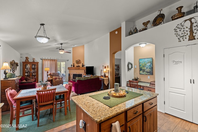 dining area featuring arched walkways, ceiling fan, a fireplace, and light wood-style floors