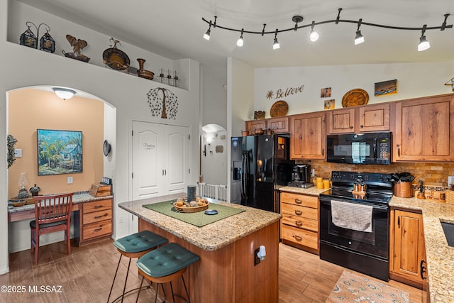 kitchen featuring arched walkways, brown cabinets, black appliances, decorative backsplash, and a kitchen island