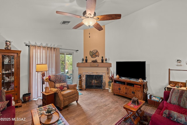 living room featuring visible vents, ceiling fan, wood finished floors, vaulted ceiling, and a lit fireplace