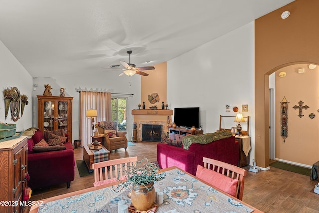 living room with arched walkways, ceiling fan, wood finished floors, a tile fireplace, and lofted ceiling