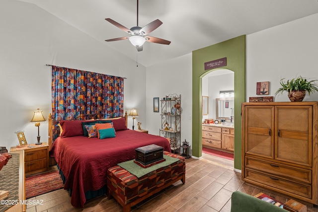 bedroom featuring light wood-style flooring, connected bathroom, arched walkways, and vaulted ceiling