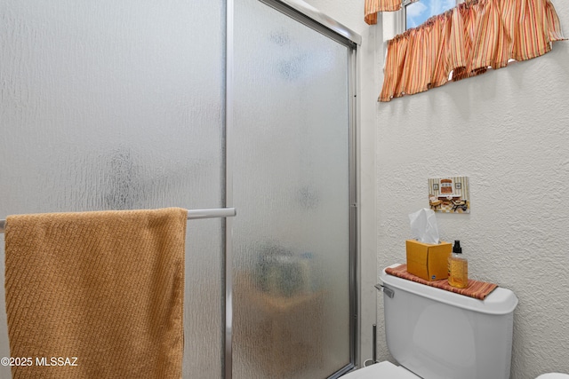 bathroom with a textured wall, toilet, and a stall shower