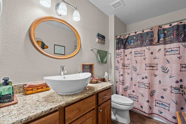 full bathroom featuring visible vents, toilet, a textured wall, vanity, and wood finished floors