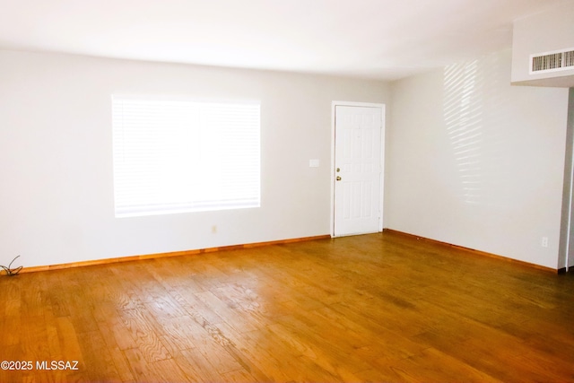 unfurnished room featuring baseboards, visible vents, and wood finished floors