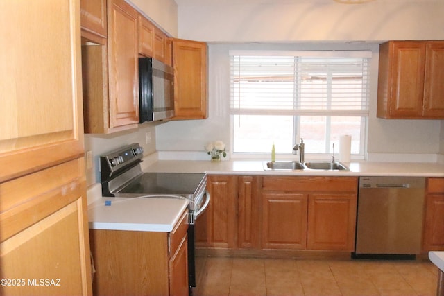 kitchen with light countertops, light tile patterned floors, stainless steel appliances, a sink, and brown cabinetry