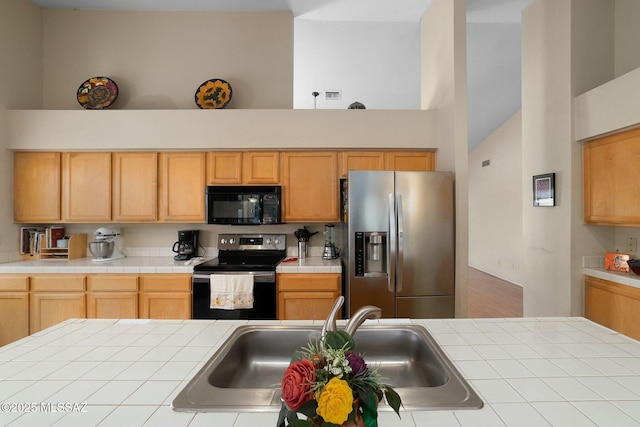 kitchen with stainless steel refrigerator with ice dispenser, range with electric stovetop, a sink, black microwave, and tile countertops