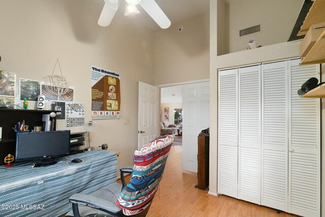 home office with wood finished floors, ceiling fan, a towering ceiling, and visible vents