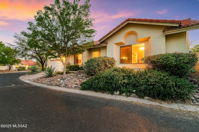 view of front of house with a tiled roof, concrete driveway, a garage, and stucco siding