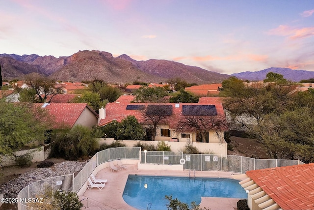 pool at dusk featuring a patio, a mountain view, and fence