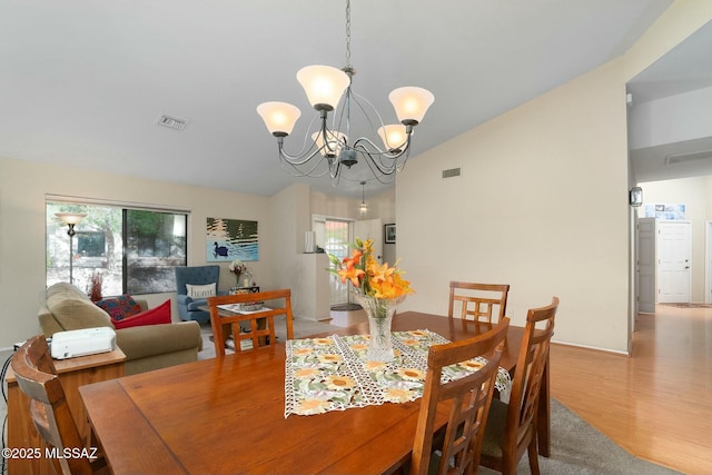 dining room with visible vents, wood finished floors, a notable chandelier, and vaulted ceiling