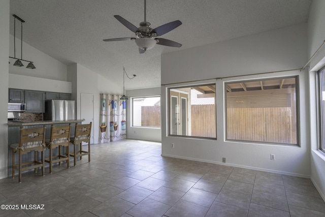 unfurnished living room featuring tile patterned floors, high vaulted ceiling, a textured ceiling, baseboards, and ceiling fan