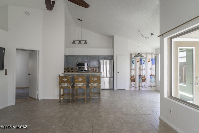 kitchen with lofted ceiling, stainless steel appliances, gray cabinetry, hanging light fixtures, and a ceiling fan