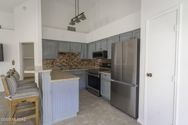kitchen featuring a breakfast bar area, gray cabinetry, a sink, visible vents, and appliances with stainless steel finishes