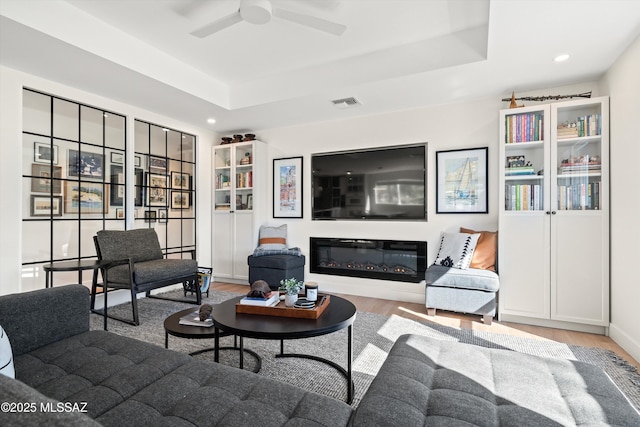 living area with a ceiling fan, wood finished floors, a raised ceiling, visible vents, and recessed lighting