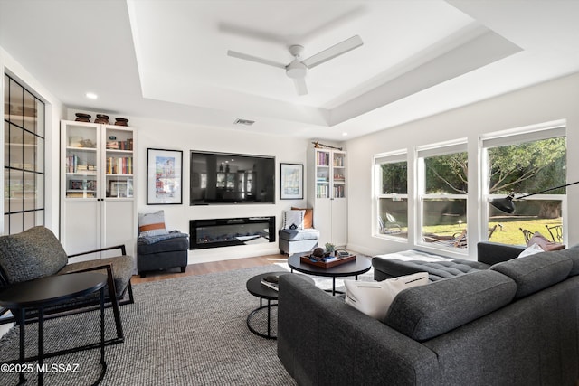 living room with recessed lighting, a raised ceiling, wood finished floors, visible vents, and a ceiling fan