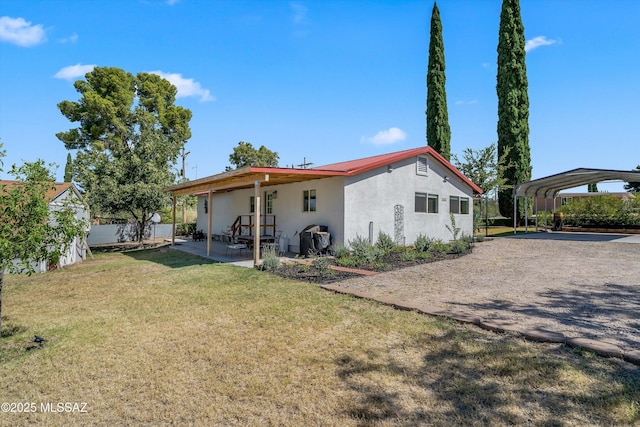 rear view of house featuring dirt driveway, stucco siding, a carport, a lawn, and metal roof