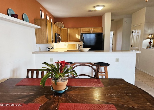 kitchen with visible vents, a peninsula, stainless steel microwave, light tile patterned floors, and freestanding refrigerator