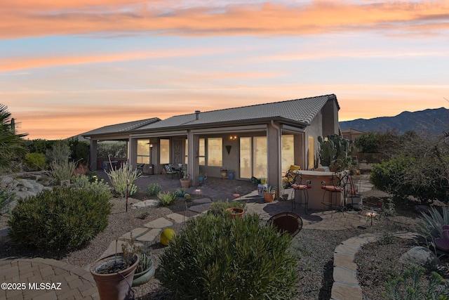 rear view of house with a patio area, outdoor dry bar, a mountain view, a tiled roof, and stucco siding