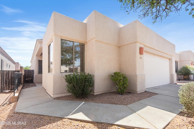 view of front of house featuring stucco siding, driveway, a garage, and fence