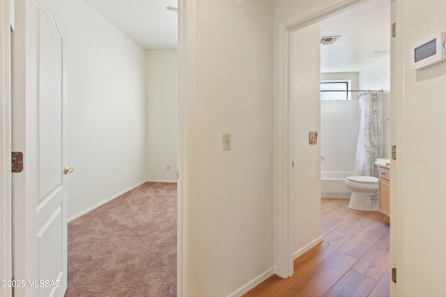 hall with baseboards, light wood-style floors, light colored carpet, and visible vents