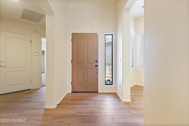entryway with arched walkways, baseboards, light wood finished floors, and visible vents
