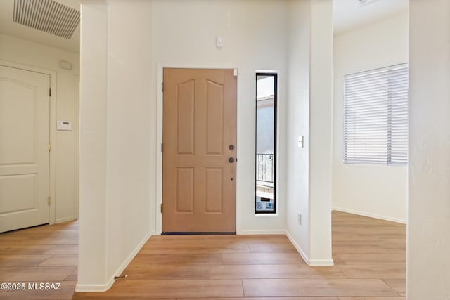 foyer with light wood finished floors, baseboards, and visible vents