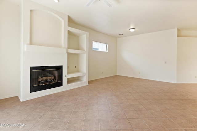 unfurnished living room with built in features, baseboards, a glass covered fireplace, and light tile patterned flooring