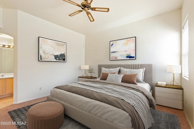 bedroom featuring baseboards, connected bathroom, ceiling fan, and light carpet