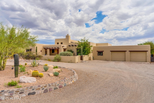 pueblo-style house with stucco siding, an attached garage, and dirt driveway