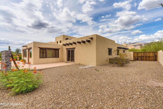 rear view of house with stucco siding, a gate, fence, and a patio area