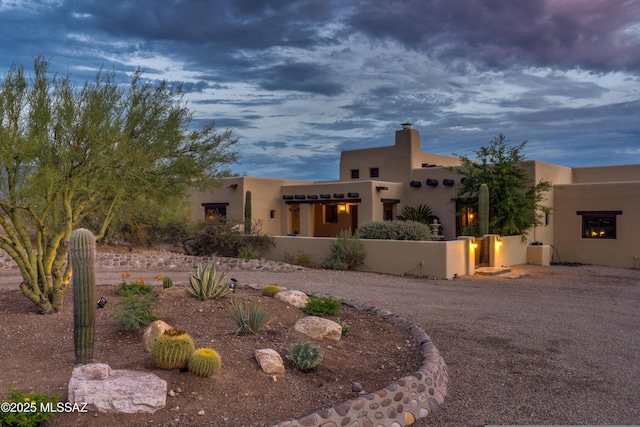 pueblo-style house with stucco siding, a chimney, and a fenced front yard