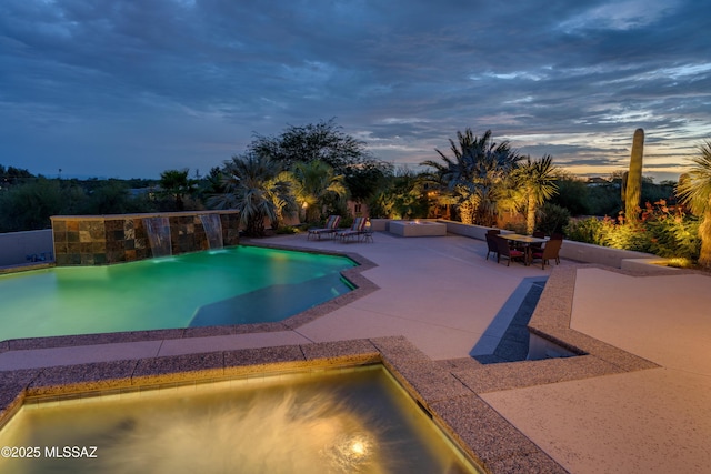 pool at dusk featuring a hot tub, an outdoor pool, an outdoor fire pit, and a patio area
