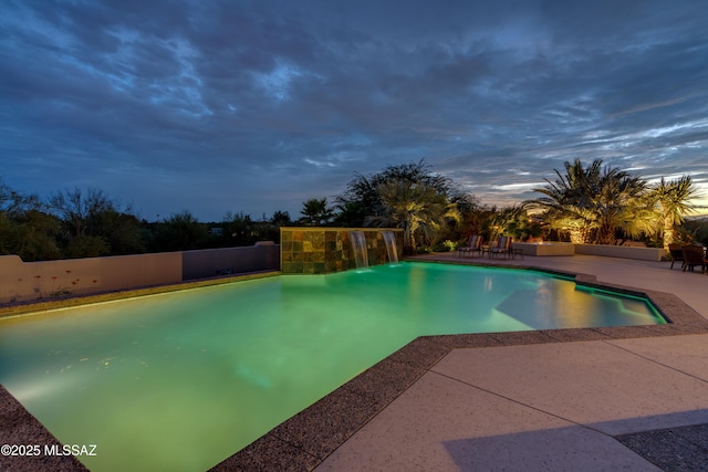 pool at dusk with an outdoor pool, fence, and a patio area