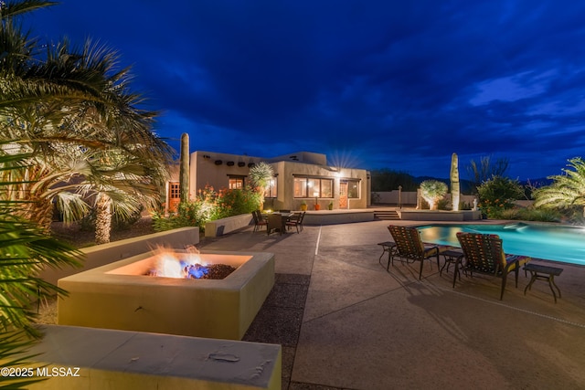 patio at twilight featuring an outdoor pool and a fire pit