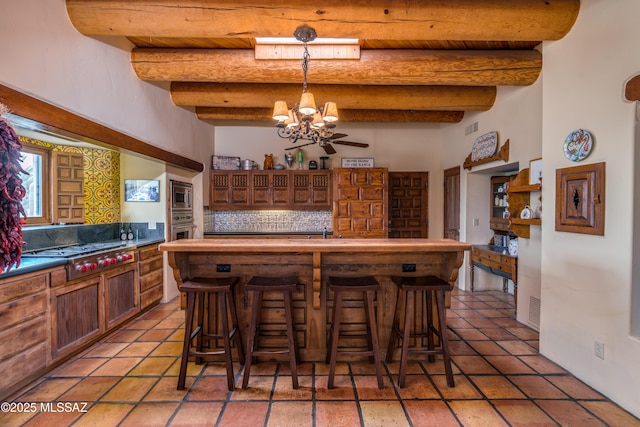 kitchen with a notable chandelier, beam ceiling, backsplash, a breakfast bar area, and stainless steel appliances