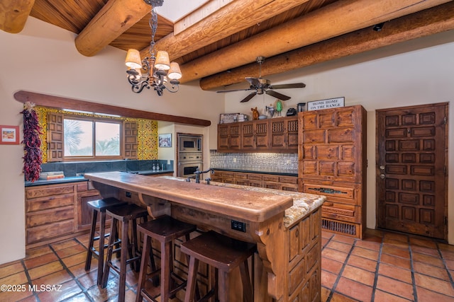 kitchen featuring beam ceiling, a kitchen breakfast bar, appliances with stainless steel finishes, a center island with sink, and decorative backsplash