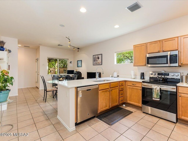 kitchen featuring appliances with stainless steel finishes, light tile patterned floors, a peninsula, and a sink