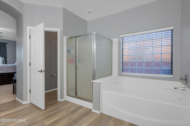 bathroom featuring a bath, a shower stall, wood finished floors, and baseboards