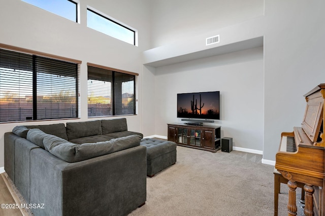 living area with a towering ceiling, visible vents, carpet, and baseboards