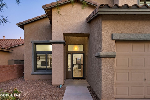 property entrance with a tile roof, a garage, stucco siding, and fence