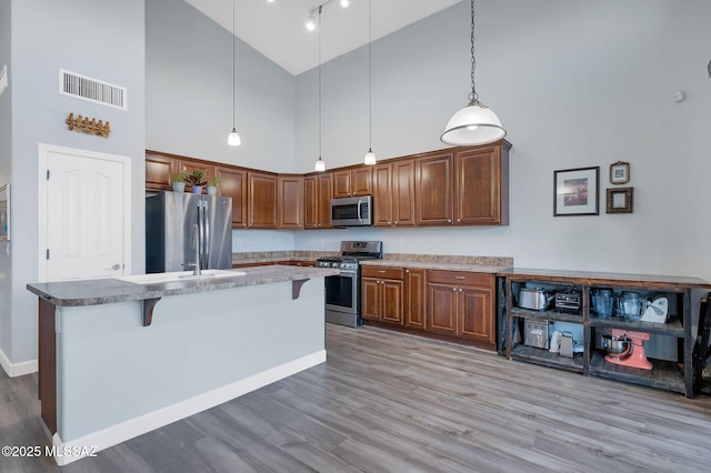 kitchen featuring appliances with stainless steel finishes, visible vents, light wood-type flooring, a kitchen island with sink, and high vaulted ceiling