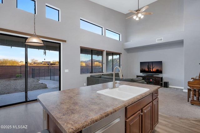 kitchen with a sink, ceiling fan, visible vents, a towering ceiling, and open floor plan