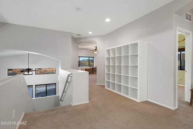 hallway with an upstairs landing, carpet flooring, and arched walkways