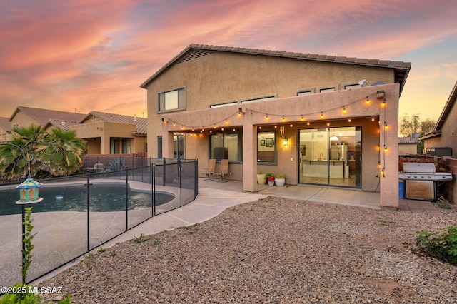 back of house at dusk with fence, a patio, stucco siding, and a fenced in pool