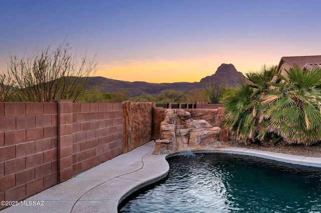 pool at dusk with a mountain view, fence, and a fenced in pool