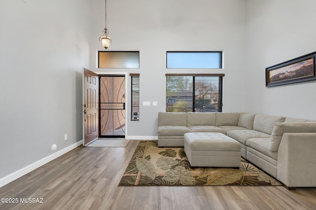 living room featuring a towering ceiling, wood finished floors, and baseboards
