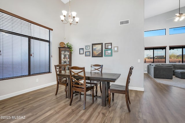 dining space featuring a towering ceiling, visible vents, wood finished floors, and baseboards