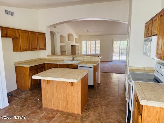 1370 N Birds Nest Rd, Green Valley, AZ 85614 - kitchen with brown cabinetry, arched walkways, a sink, a peninsula, and white appliances