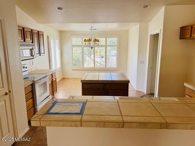 1370 N Birds Nest Rd, Green Valley, AZ 85614 - kitchen featuring white electric range oven, tile counters, brown cabinetry, and a notable chandelier