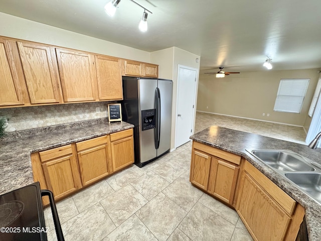 kitchen featuring stainless steel refrigerator with ice dispenser, decorative backsplash, a sink, dark countertops, and a ceiling fan